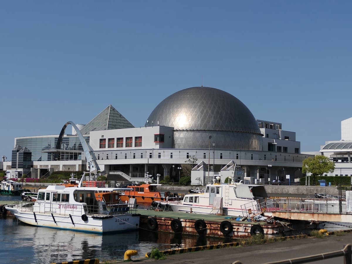 The Port of Nagoya Public Aquarium's silver dome buildings beside the harbor with boats moored in front