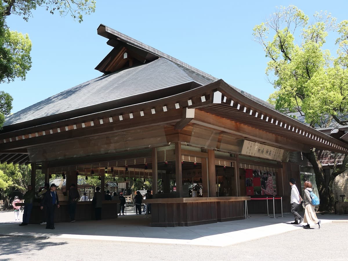 A large wooden hall with a sweeping roof in the grounds of Atsuta Jingu, with visitors in front