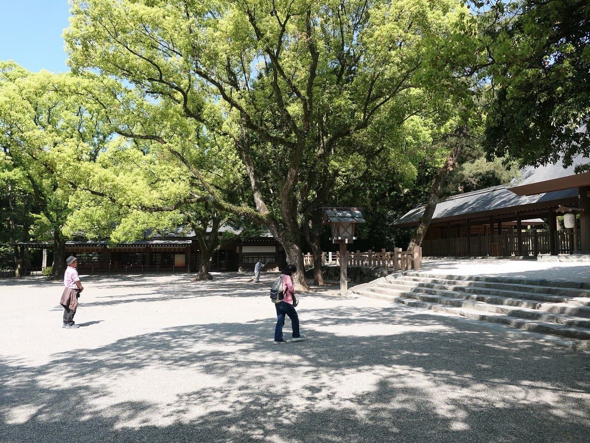 Visitors walking across the wide gravel grounds of Atsuta Jingu under large camphor trees