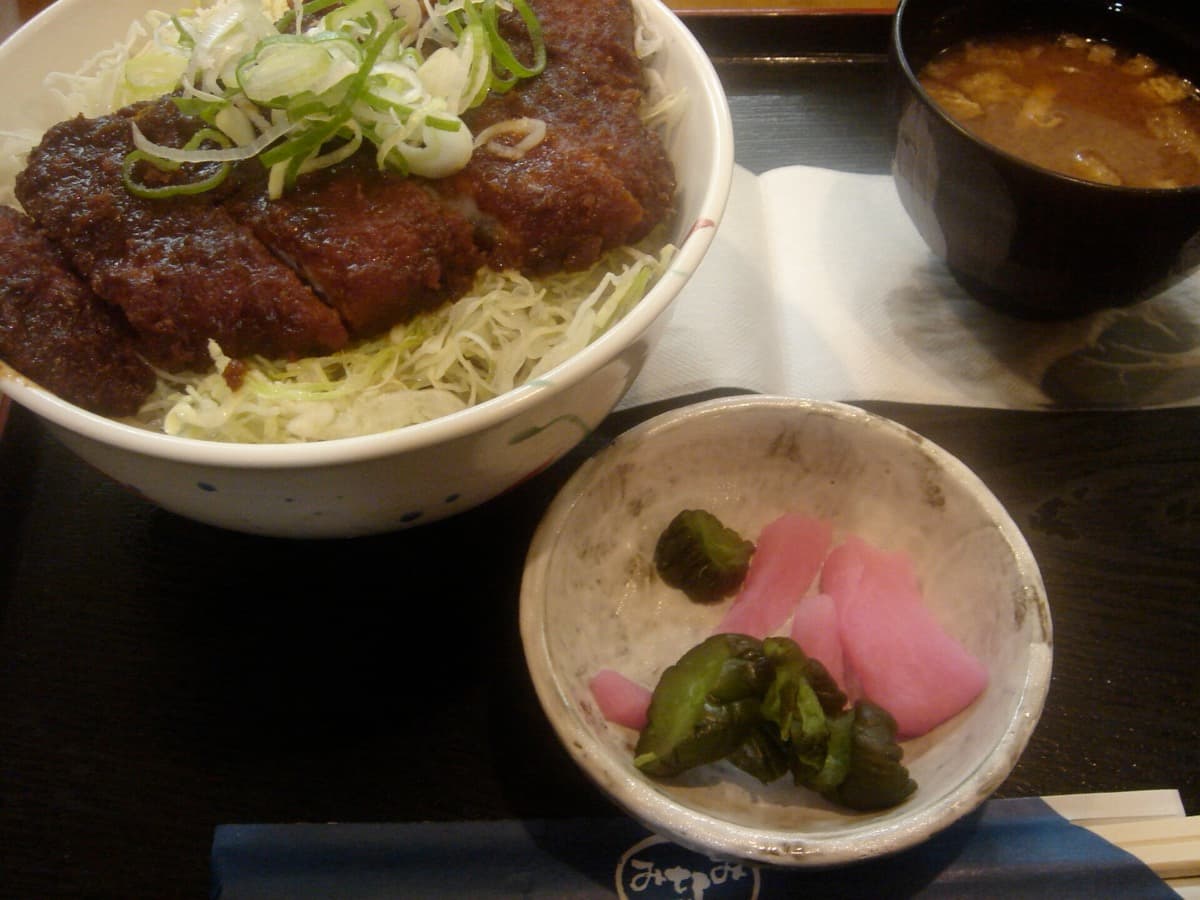 A pork cutlet in dark miso sauce over shredded cabbage with pickles and miso soup