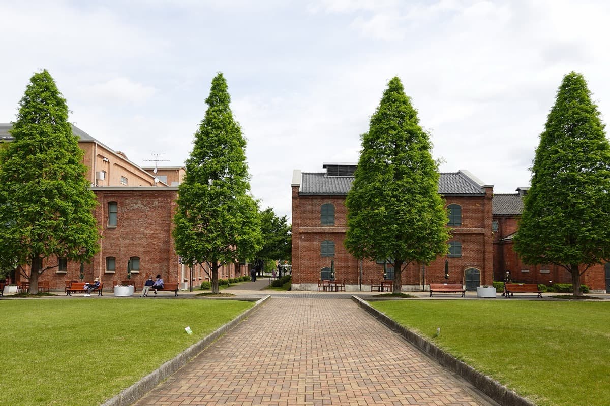 Red-brick buildings, lawns and conical trees along a brick path at Noritake Garden