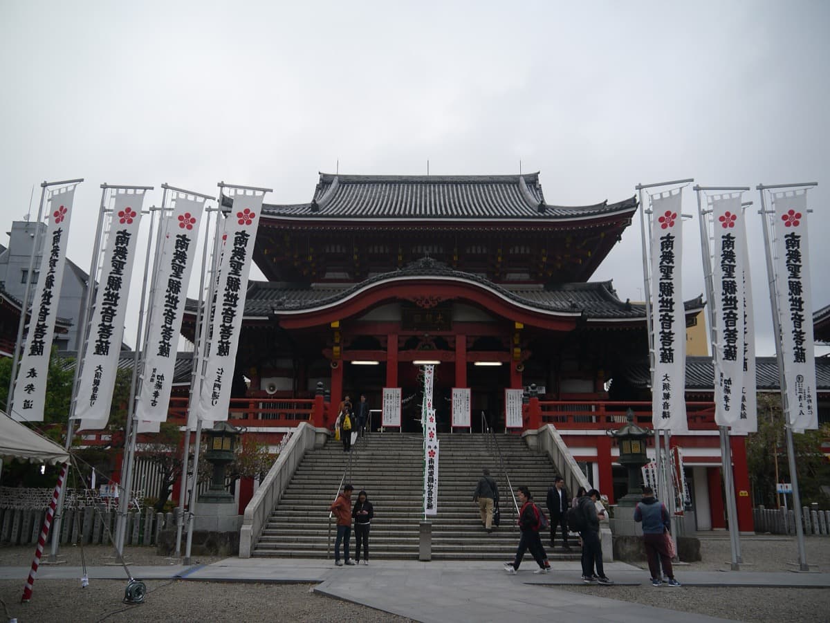 The red main hall of Osu Kannon temple with white banners on either side of the steps