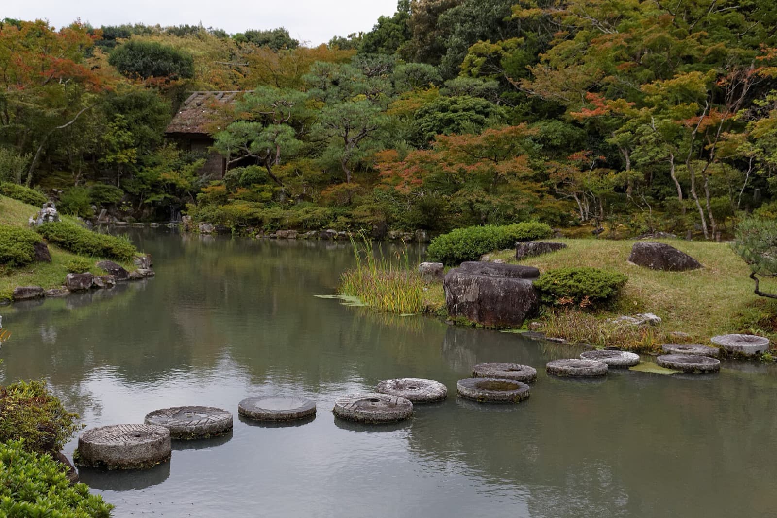 Round stepping stones crossing a still pond toward a pine-covered island at Isuien Garden in Nara
