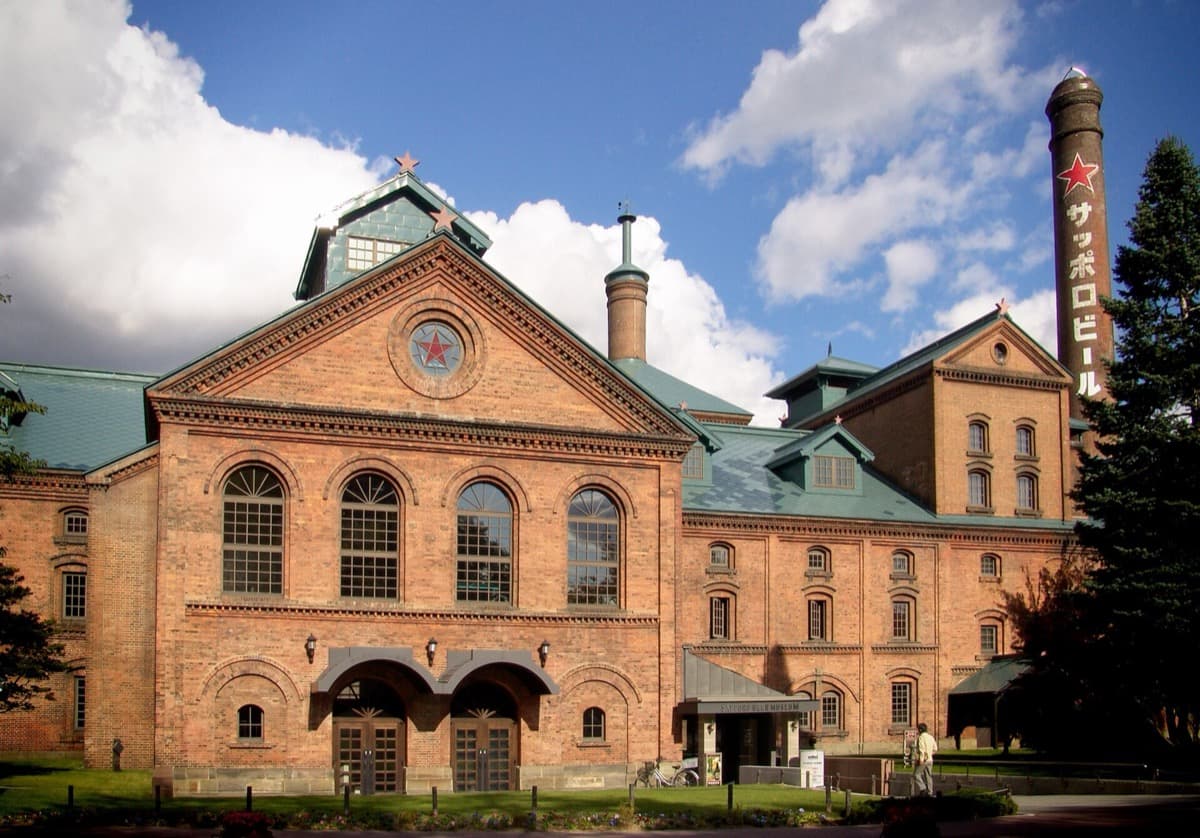 The red-brick Sapporo Beer Museum with a tall chimney and green roofs under a blue sky