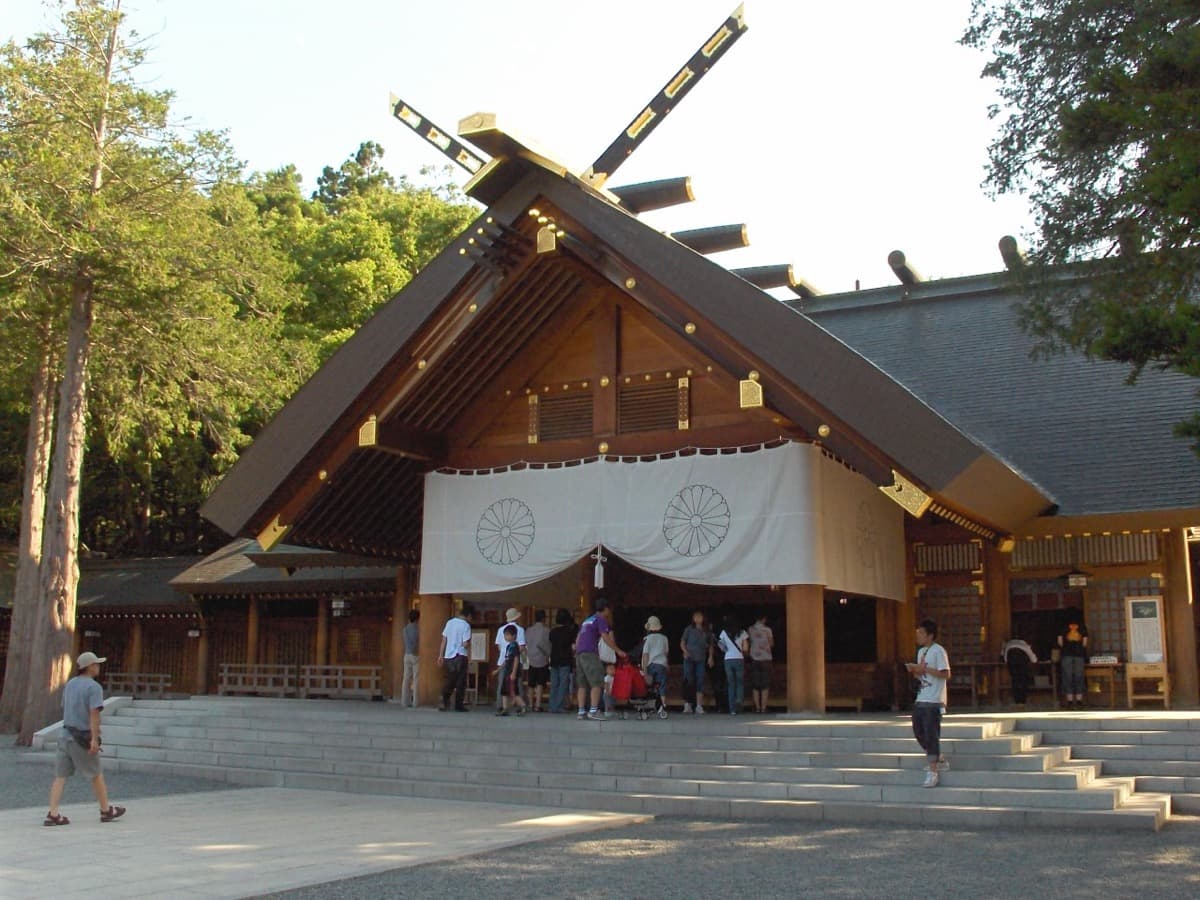 The wooden main hall of Hokkaido Jingu with white curtains and worshippers on the steps