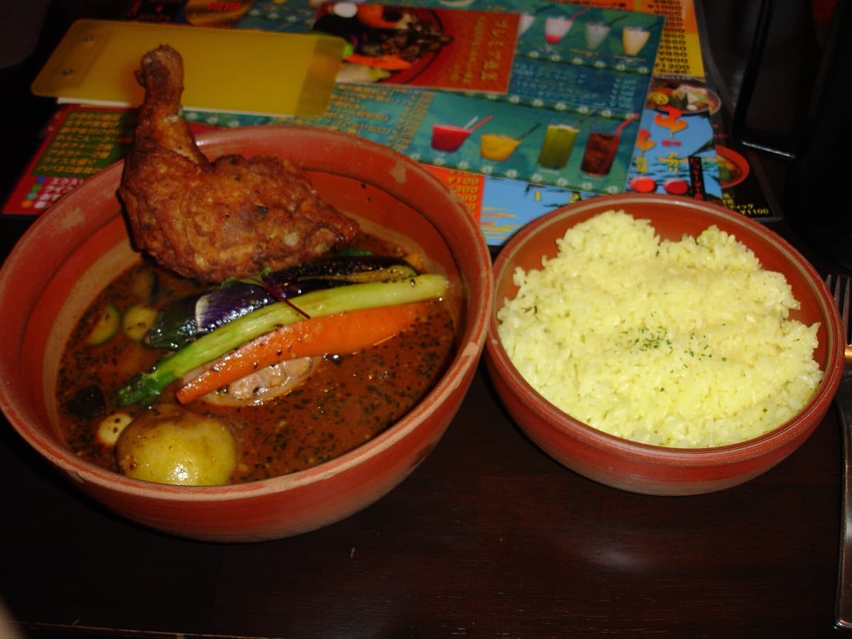 Soup curry with a chicken leg and roast vegetables next to a bowl of yellow rice at a Sapporo restaurant