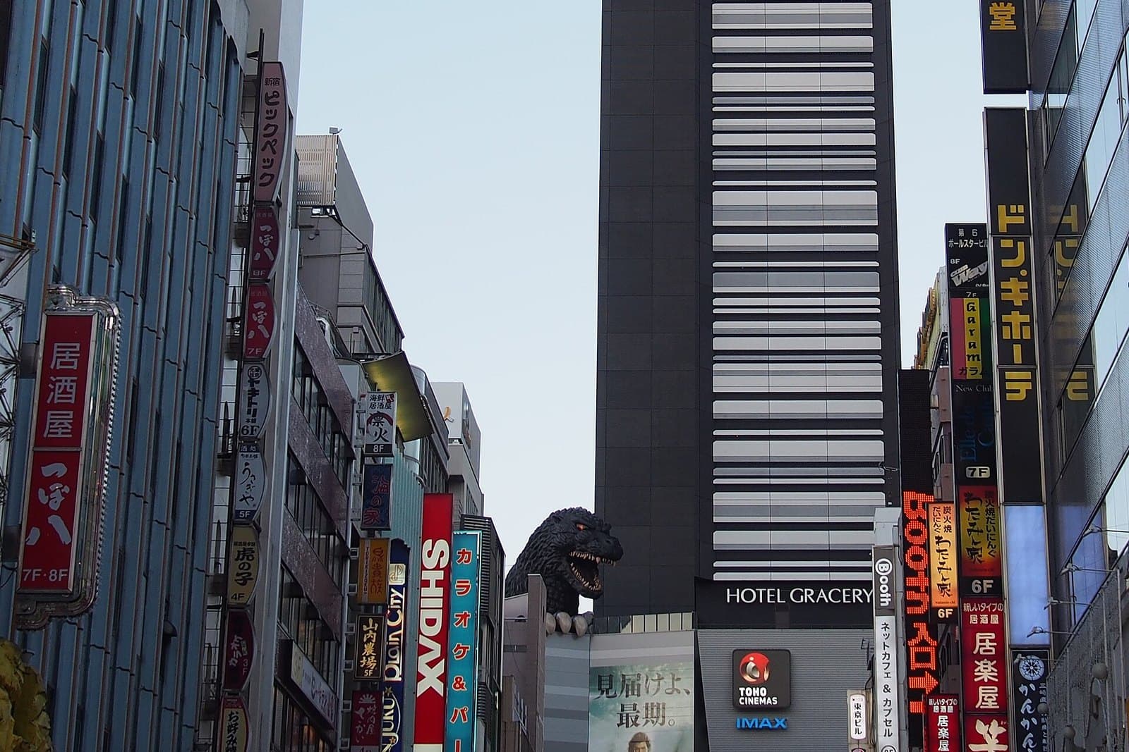 The Godzilla head on the Shinjuku Toho Building next to the Hotel Gracery tower, seen from a Kabukicho street lined with signs