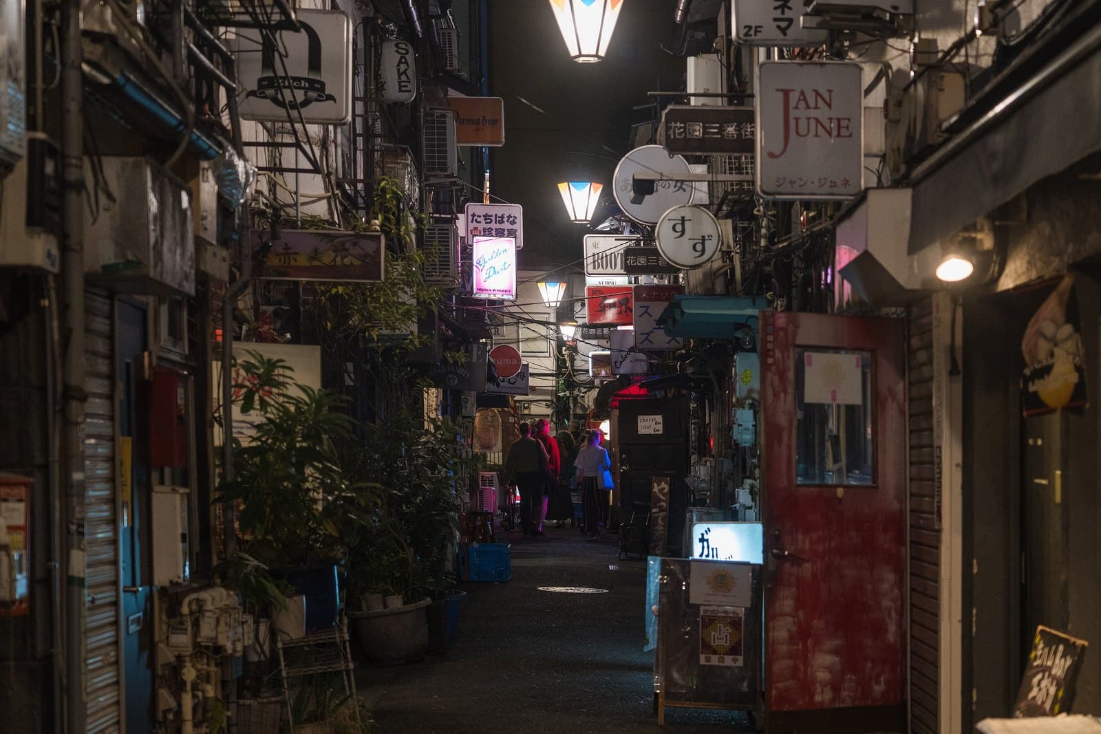 A narrow lane in Shinjuku Golden Gai at night lined with tiny bars, signs and plants
