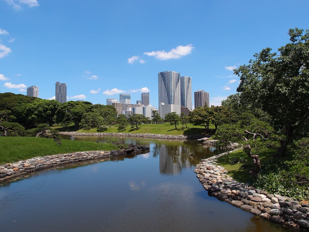 A pond with stone edges in Hamarikyu Gardens, with Shiodome's office towers behind the trees