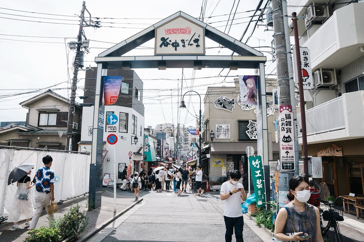 The sign gate at the entrance of the Yanaka Ginza shopping street with shoppers walking under it