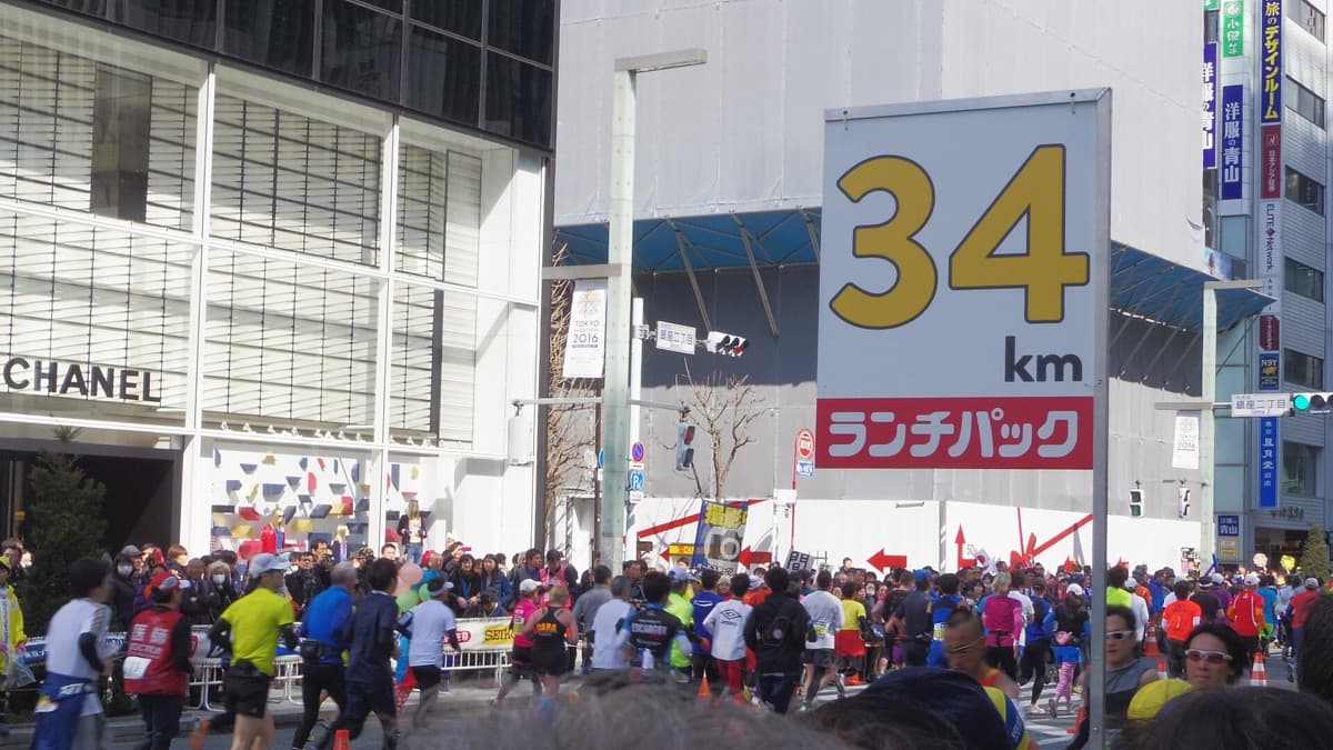 Crowds of runners on Ginza's main street between luxury shops, with spectators behind the barriers
