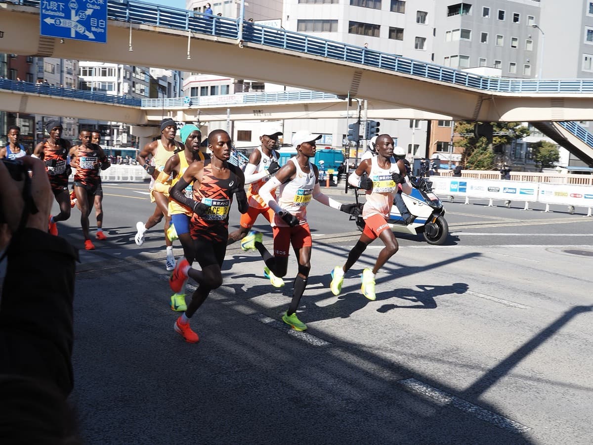 The elite lead pack of the Tokyo Marathon running under a pedestrian bridge in the early kilometers