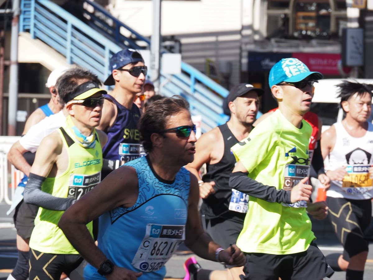 A tightly packed group of marathon runners in bright tops and caps running on a Tokyo street