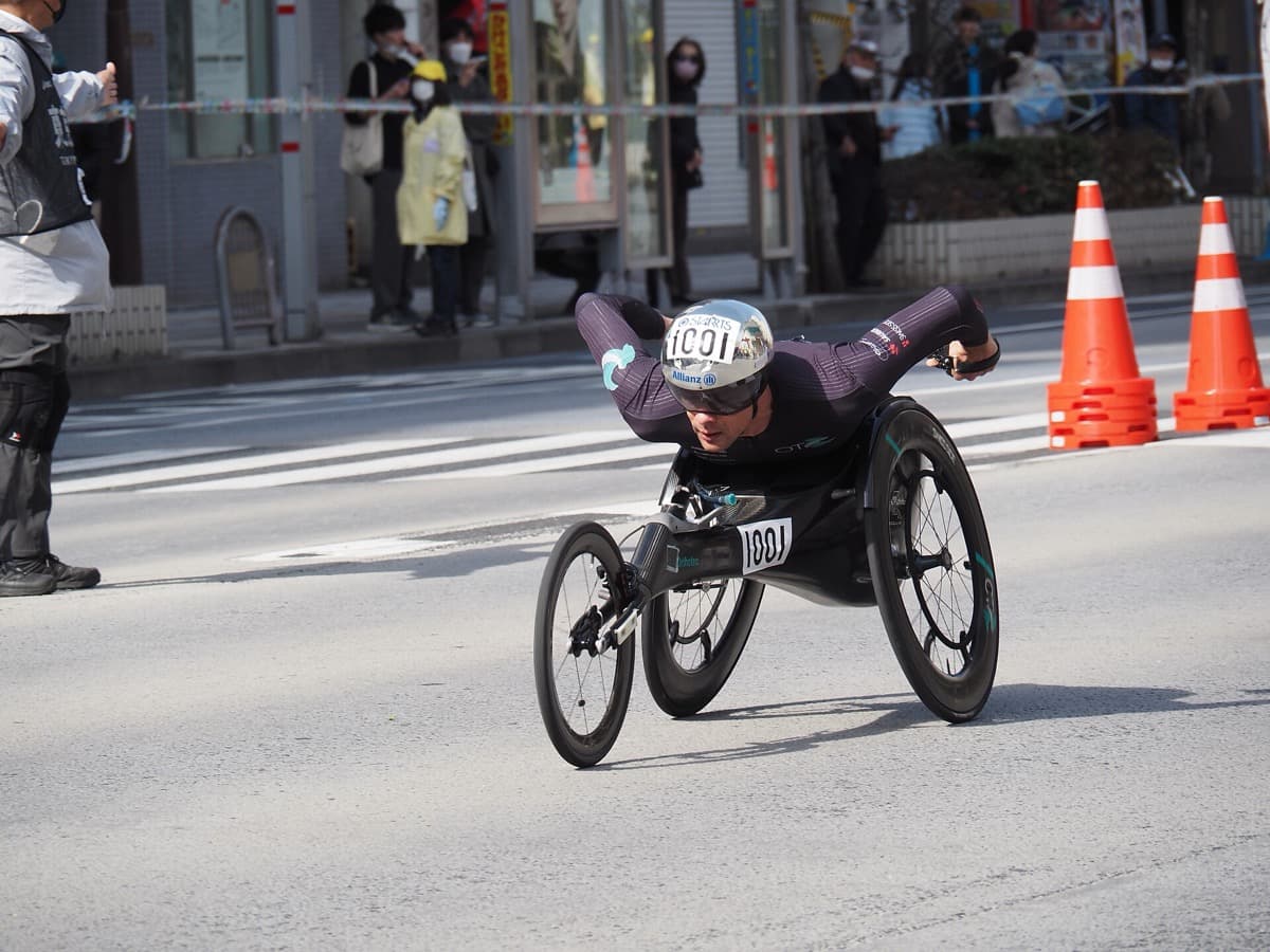 A wheelchair racer in a racing chair leaning forward on a Tokyo street lined with traffic cones