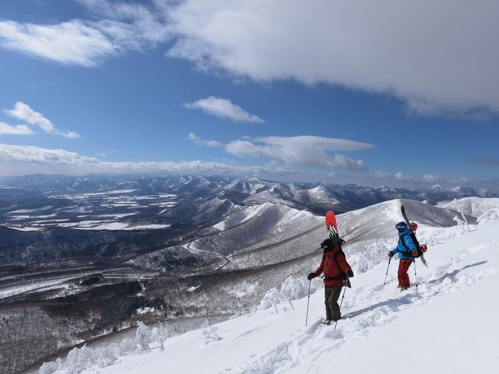 Two riders hiking a snow-covered ridge above a valley in central Hokkaido