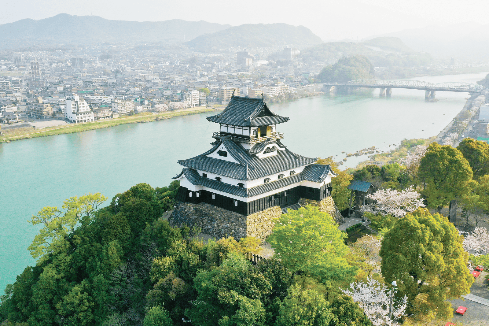 Inuyama Castle on a wooded hill above the wide Kiso River, with the town and mountains behind