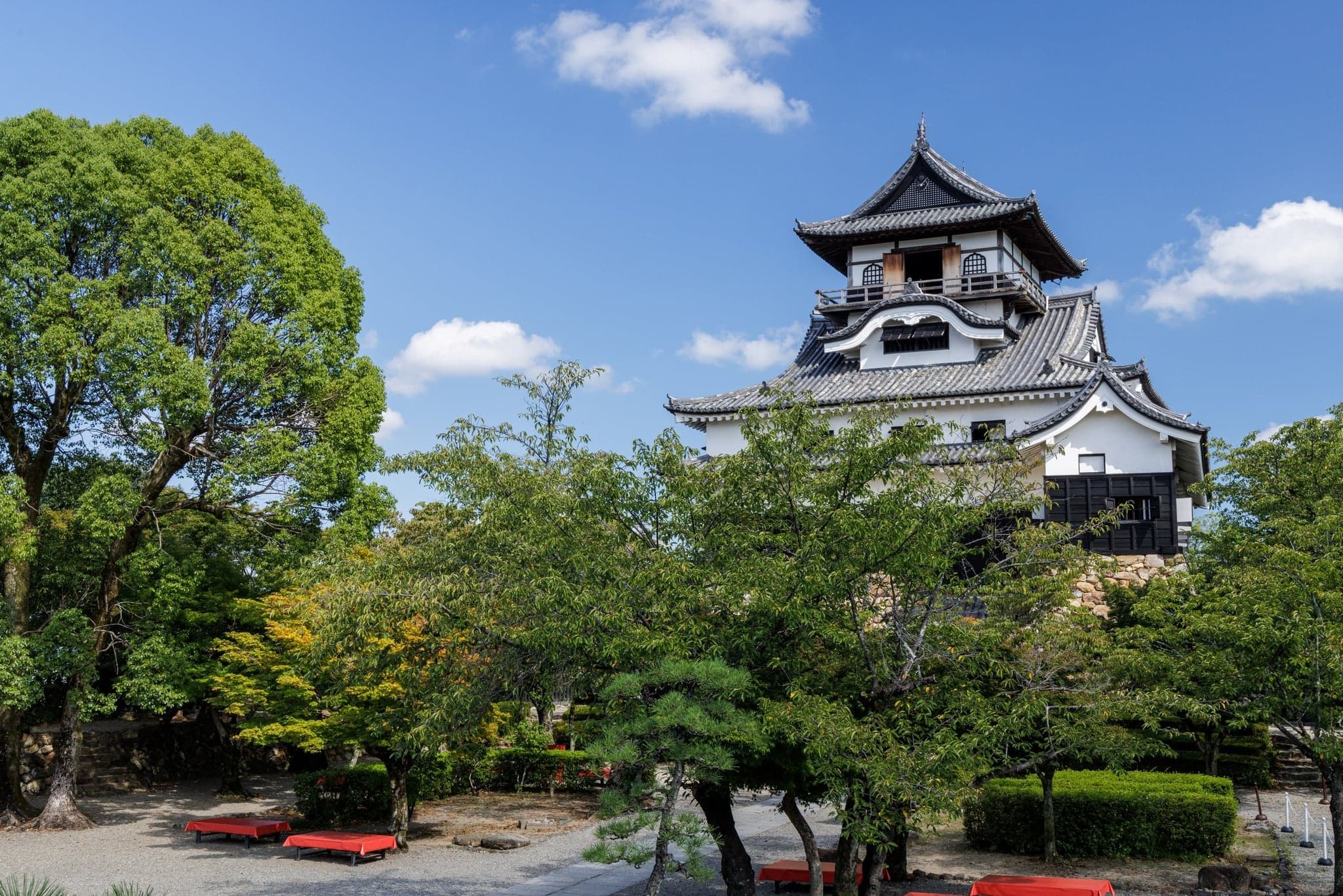 Inuyama Castle's white keep rising above green trees under a blue sky