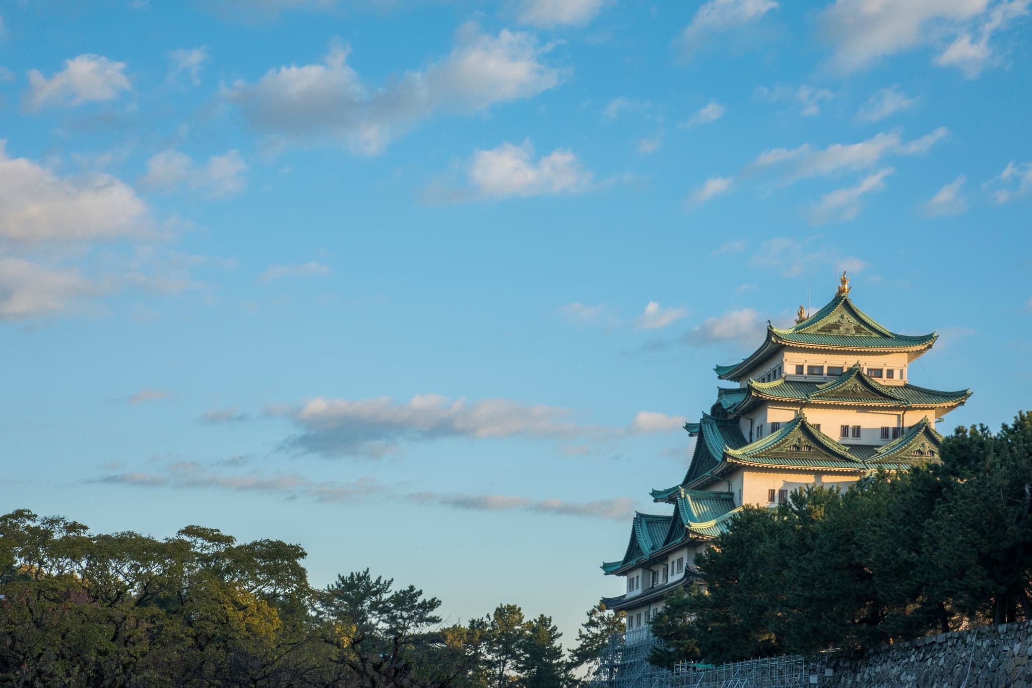Nagoya Castle's keep with its green roofs rising above trees against a blue sky with clouds