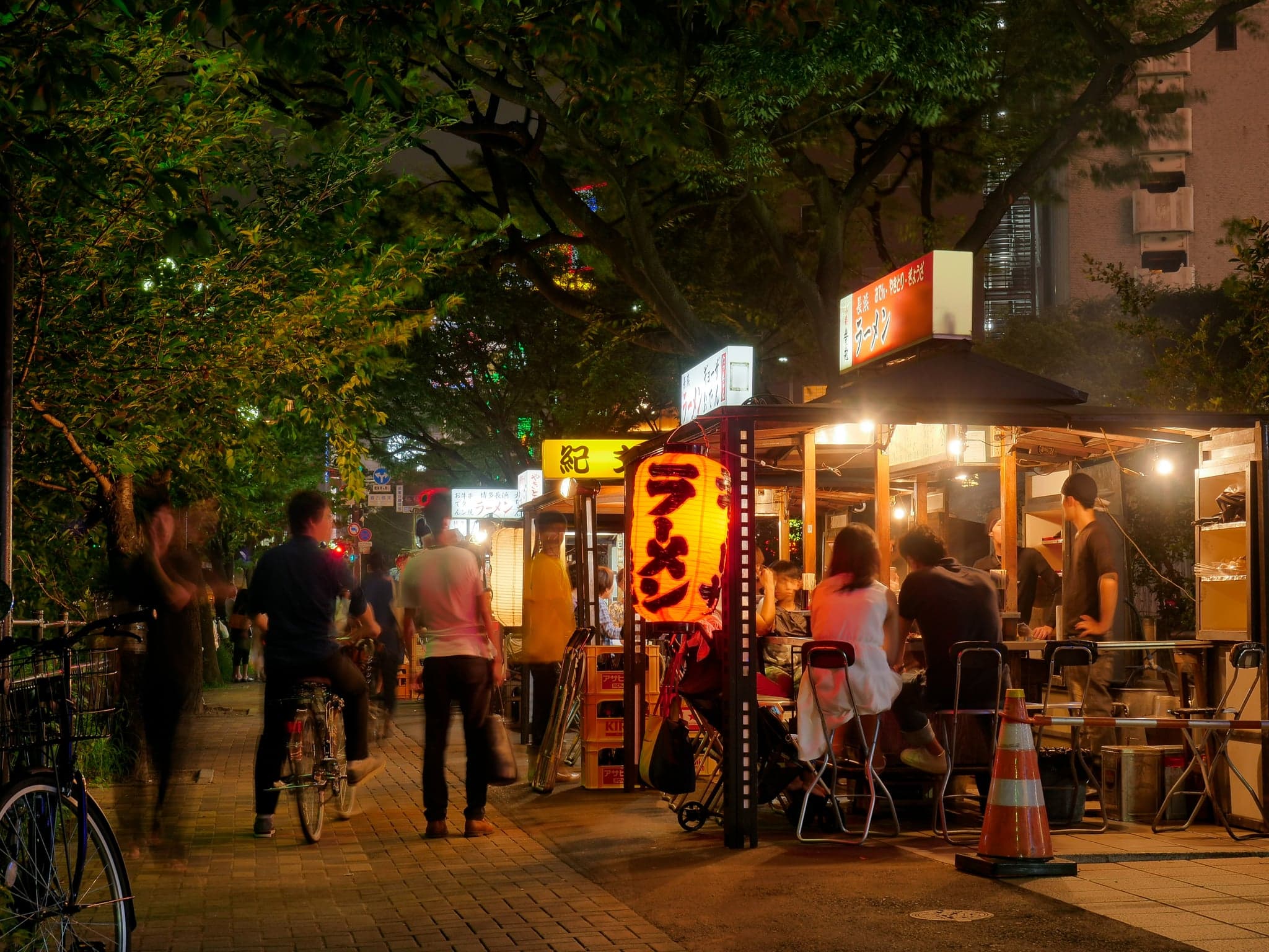 Yatai food stalls lit with lanterns under the trees at night, with customers seated at the counters