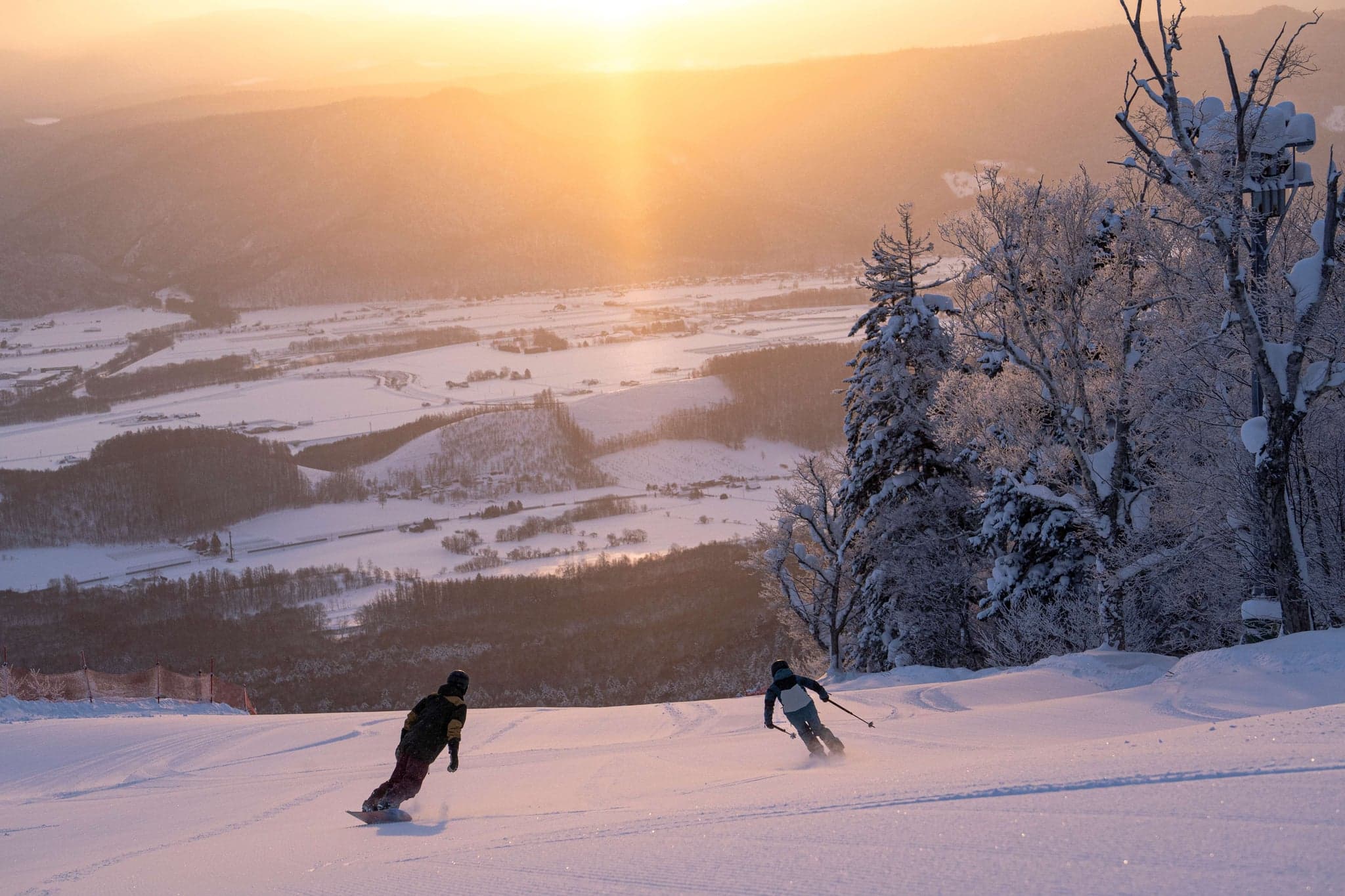 Deux snowboardeurs sur une piste de Furano au coucher du soleil