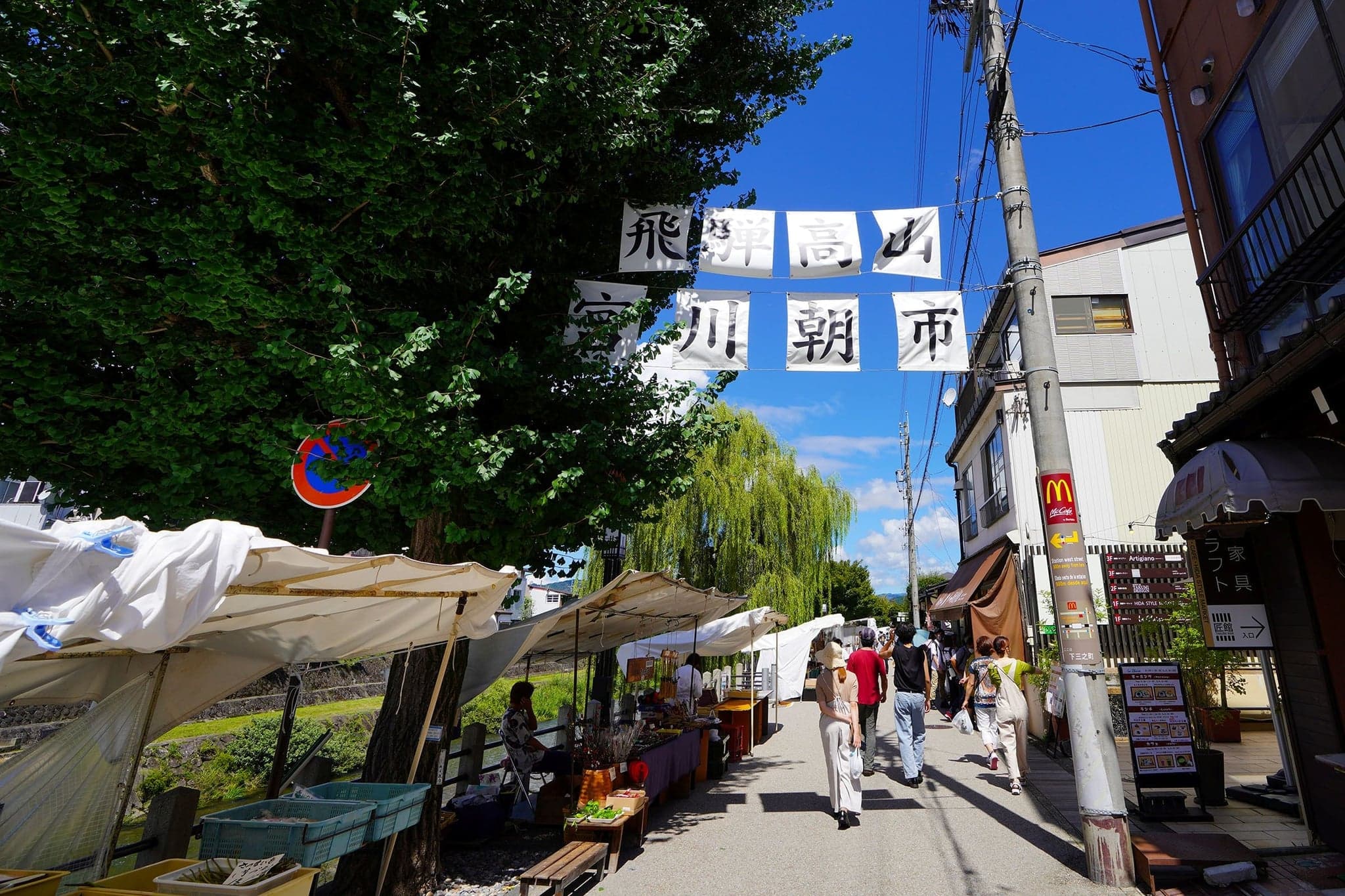 The Miyagawa morning market in Takayama, with white-canopied stalls along the riverside street under the market banner