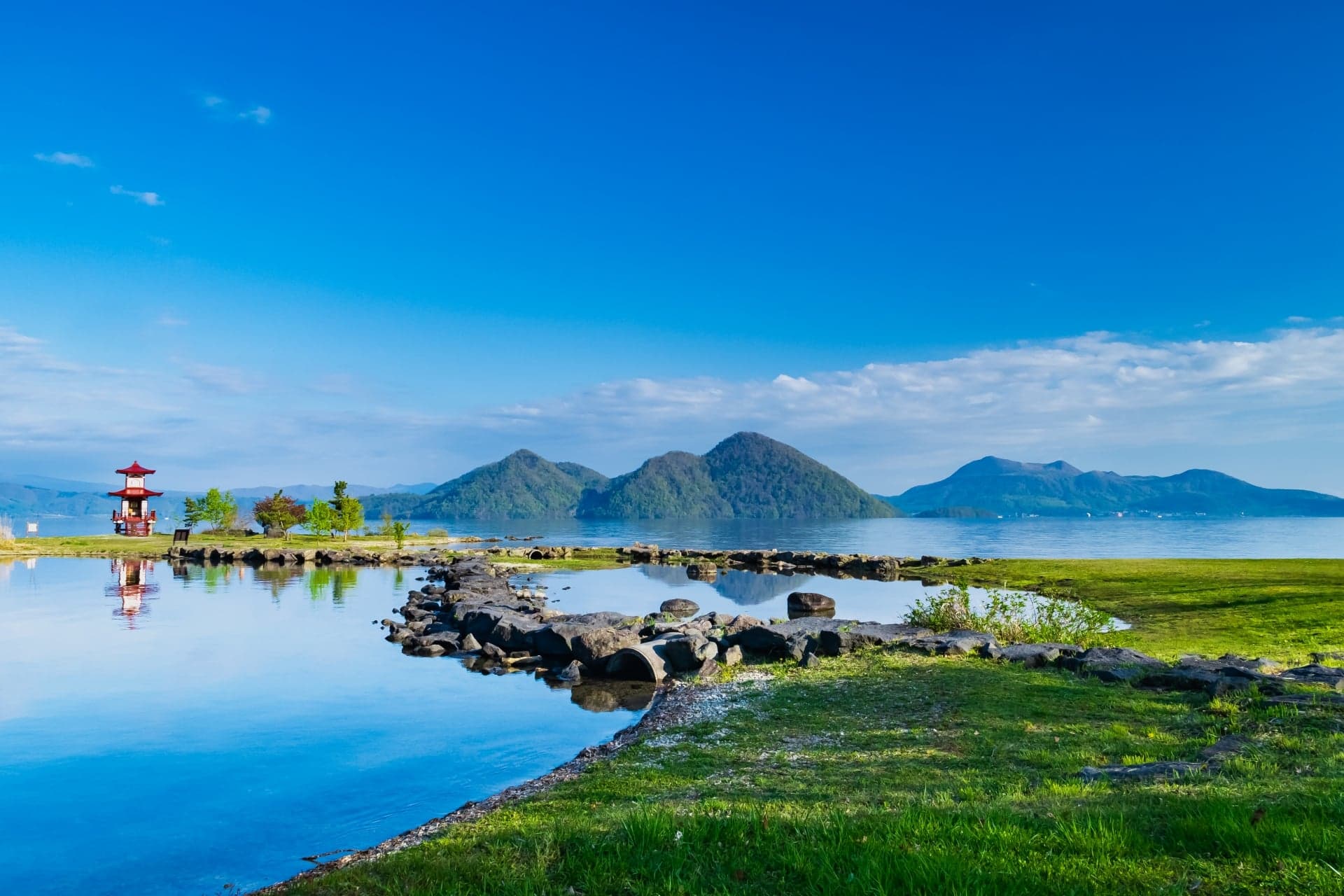Lake Toya with its wooded central islands and a small lighthouse on the shore under a blue sky
