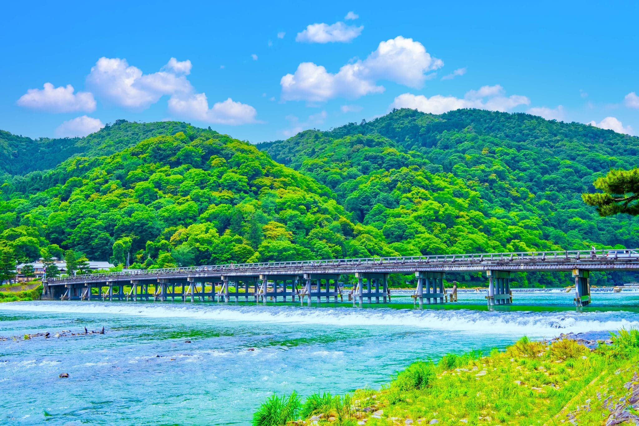Togetsukyo Bridge crossing a wide river below green wooded hills in Arashiyama
