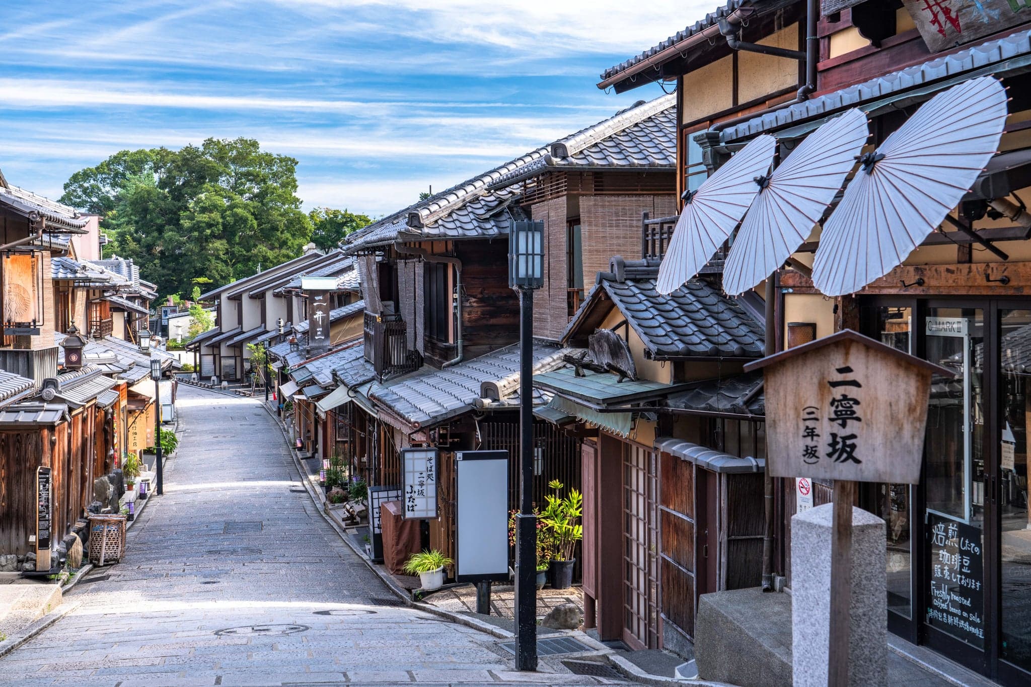 Ninenzaka in Kyoto: a stone-paved slope lined with two-storey wooden shops, paper umbrellas and a wooden street sign
