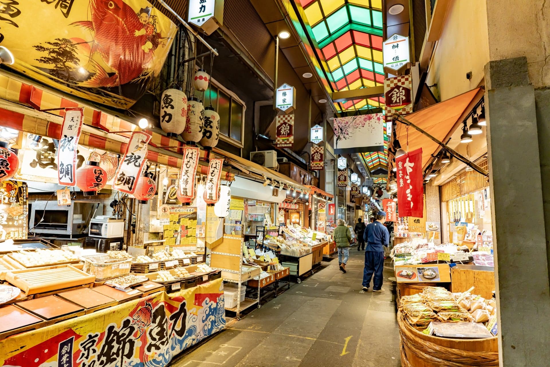 Food stalls and shop signs under the coloured glass roof of Nishiki Market in Kyoto
