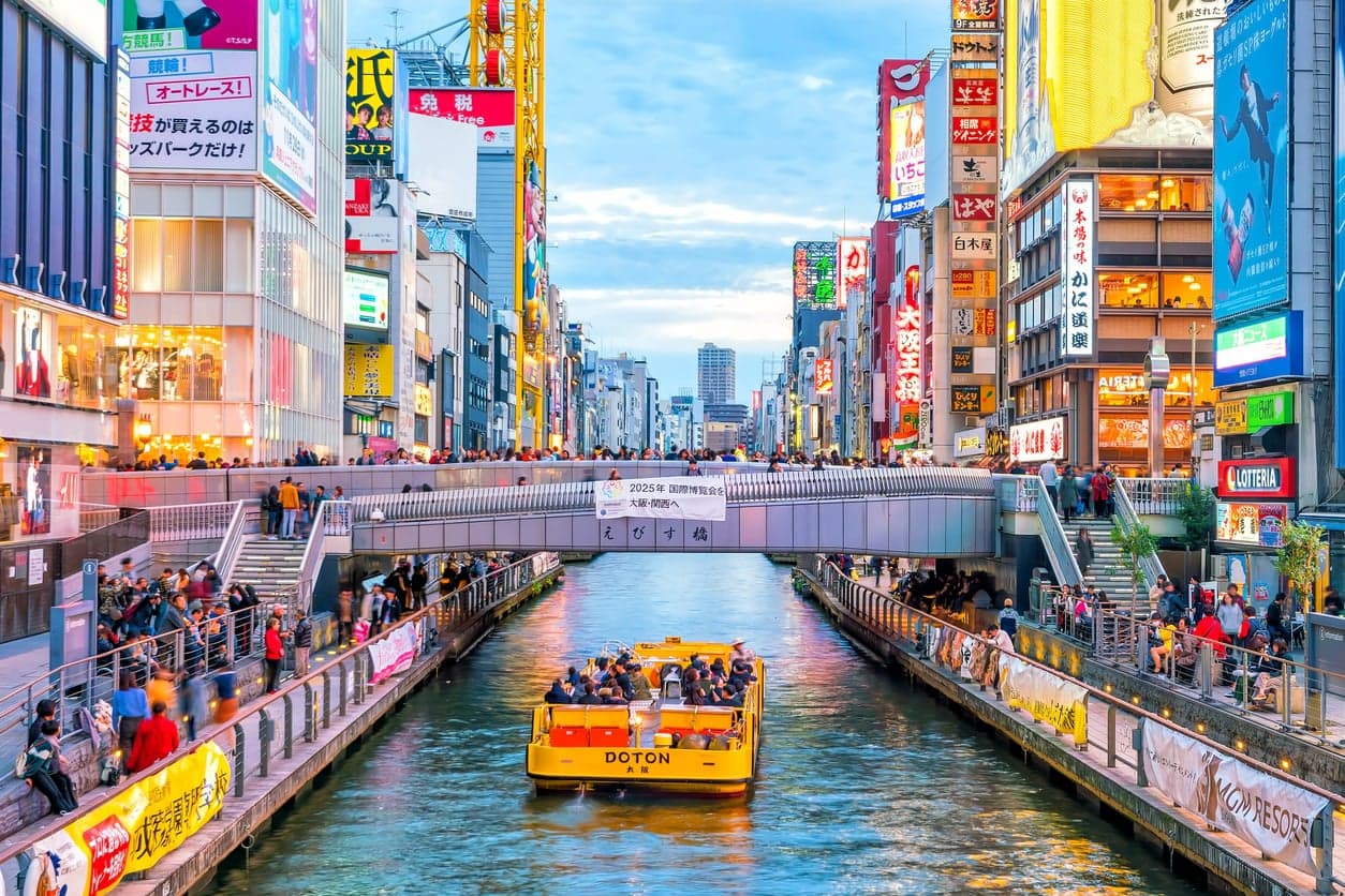 El canal de Dotonbori en Osaka con un barco turístico amarillo y paseos llenos de letreros de neón gigantes