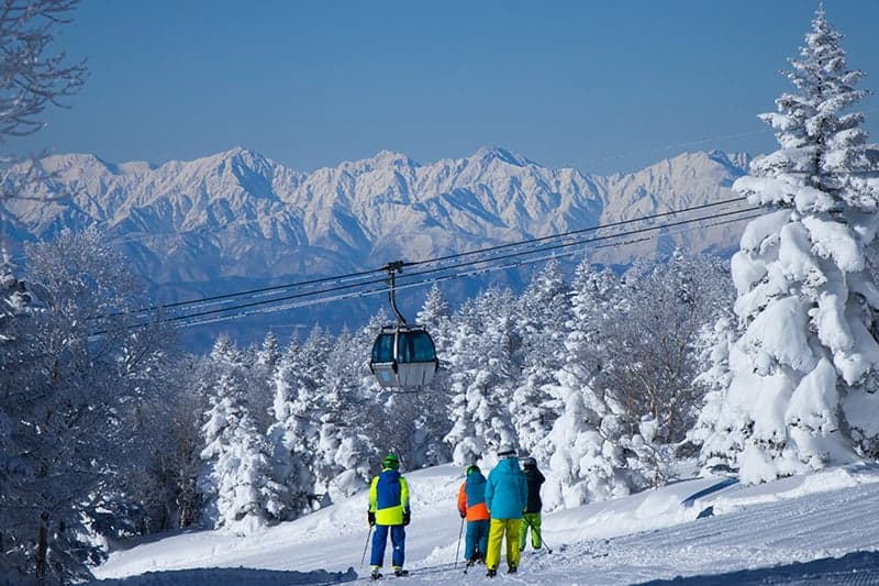 Eine Gondel über verschneiten Bäumen und Skifahrern in Shiga Kogen