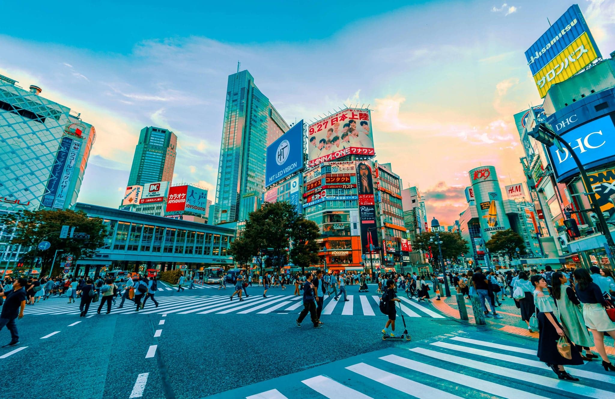 People crossing the Shibuya Scramble Crossing in daylight under tall buildings with screens