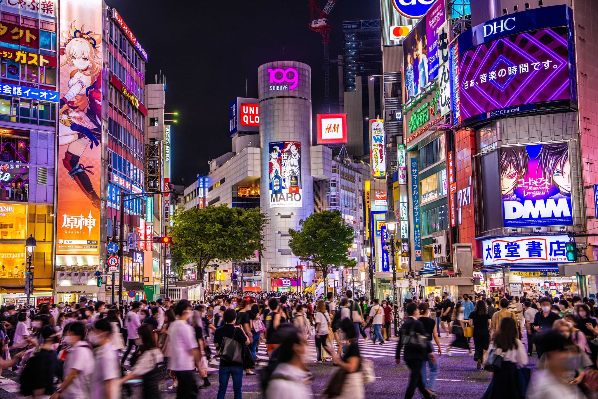 Shibuya at night with crowds under bright neon screens and the 109 building