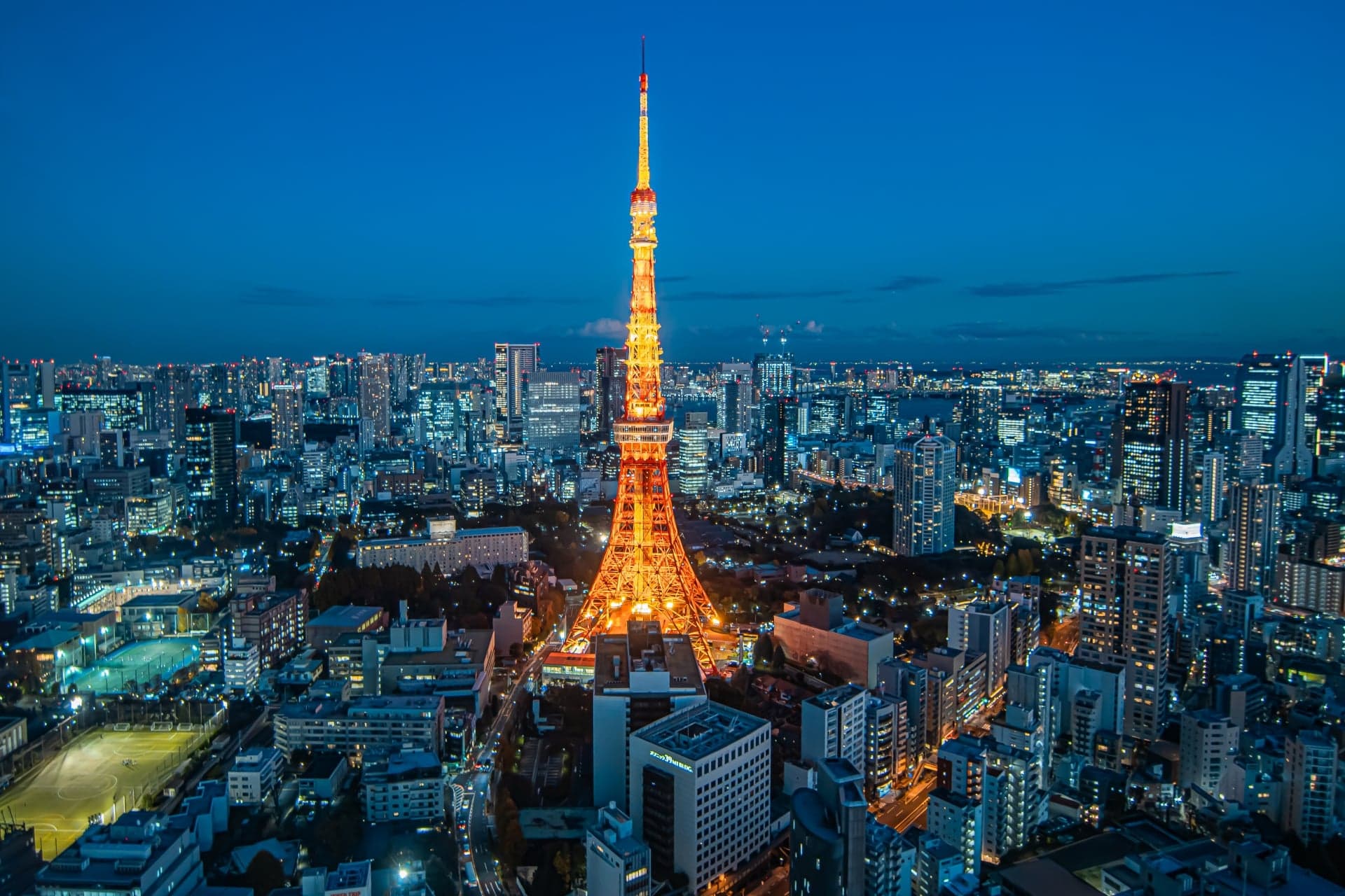 Tokyo Tower lit in orange at dusk, rising above the surrounding city